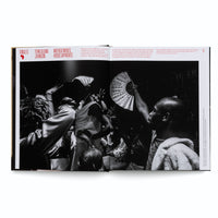 An open book displays a large, black and white photograph of a vibrant and crowded party. In a dimly lit room, a group of Black people are dancing energetically with their arms raised. In the foreground, one person holds a large, decorated fan high in the air, while others are captured in expressive, joyful motion.