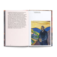 A photograph of an open art book. The left page contains German text. The right page displays Edvard Munch's 1906 expressionist painting of Friedrich Nietzsche. The portrait shows the philosopher in a dark suit standing on a bridge, overlooking a swirling, colorful landscape with a yellow sky.