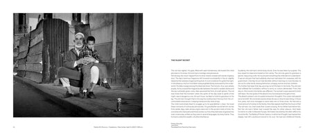 A two-page book spread. On the left, a black and white photograph shows an elderly man with a white beard and cap holding a young boy on his lap. They sit together on a curb in front of a building with a corrugated metal wall. The right page contains a story titled THE SILENT SECRET.