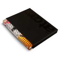 A coffee table book with a colorful, spotted spine featuring sections of orange, white, and red, is partially slid out from its matte black slipcase. The case has the words art cars embossed in a glossy black finish, with the BMW logo visible below.
