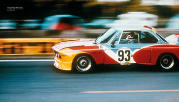 A side-profile, panning shot of the iconic Alexander Calder BMW 3.0 CSL Art Car racing at Le Mans in 1975. The number 93 car, with its bold red, yellow, and blue color-block livery, is in sharp focus, while the racetrack background is blurred to convey a powerful sense of speed.