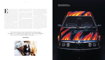 A two-page magazine spread featuring the Ernst Fuchs BMW Art Car. On the left is German text with a small photo of the artist painting. The right page shows a large, front-view studio shot of the black car, which is covered in vibrant, stylized flames of red, orange, yellow, and blue.
