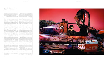 A two-page magazine spread. The left page contains columns of German text. The right page features a photograph of artist Julie Mehretu wearing sunglasses while sitting in the open cockpit of the BMW M Hybrid V8 Art Car, which has a vibrant, abstract, multicolored livery against a pink background.