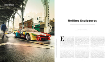 A two-page magazine spread titled Rolling Sculptures. The left page shows Andy Warhol's BMW M1 Art Car from 1979 parked on a city street in the Bronx under an elevated train track. The car is painted in vibrant, blended patches of red, yellow, green, and blue, with the number 76 on its side. The right page features the beginning of an article.