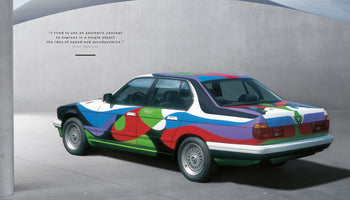 A page from a publication displays the BMW Art Car designed by César Manrique. The car, a sedan, is covered in a vibrant, flowing abstract design with large patches of blue, red, green, and purple against a minimalist grey background.