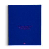 A top-down studio shot of the back of a hardcover book. The book has a textured, deep royal blue cloth cover. Centered on the cover is text in a bright pink, sans-serif font that reads: VERFASST UND HERAUSGEGEBEN VON EVA MEYER-HERMANN FÜR DEN KÜNSTLERNACHLASS JOHANNES GECCELLI. At the bottom is the publisher logo for Hatje Cantz.