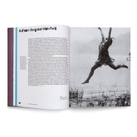 An open book showing a page of German text on the left, titled Auf dem Berg der Wahrheit, and a full-page black-and-white photograph on the right. The photo captures a person in mid-air, joyfully leaping or dancing outdoors near a body of water with reeds.