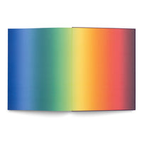 A top-down view of an open book on a white background. The pages display a continuous, smooth rainbow gradient that starts with deep blue on the left, transitions through green, yellow, and orange, and ends with a deep red on the right.
