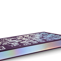 A low-angle, close-up shot of a dark purple book resting on a white surface. The cover features a pattern of stylized, graffiti-like letters with a holographic finish, and the fore-edge of the pages shimmers with an iridescent, rainbow-like effect.