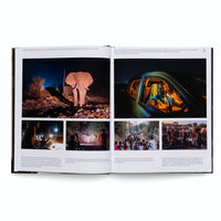 An open book displays a photo essay across two pages with French captions. The main image on the left shows an elephant standing in a landfill at night. On the right, a man sits in the warmly lit driver's seat of a car. Four smaller photos below show various scenes of local people observing and interacting with elephants in their community, both during the day and at night.