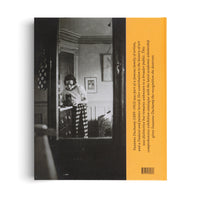 The back cover of a book about Suzanne Duchamp. The cover features a large, black and white photograph of the artist standing in a room, wearing a light-colored shirt and striped trousers. She is looking down at an object on a dresser. To the right of the photo is a vertical orange stripe containing a short biography of Duchamp and a barcode at the bottom.