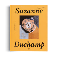 A yellow hardcover book titled Suzanne Duchamp Retrospektive, seen from a top-down perspective on a white surface. The cover features a central image of an abstract painting with a circular, geometric, fan-like shape in shades of peach, grey, and white.