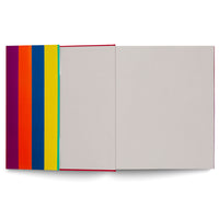 An open book laid flat against a white background, viewed from above. The back cover on the left has bold, vertical stripes of purple, orange, blue, and yellow. The book is open to two blank, light gray pages, with a thin red edge from the cover visible at the spine.