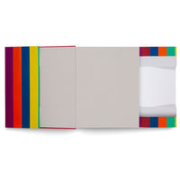 A colorful book and slipcase set laid horizontally on a white background. The cover on the left has bold vertical stripes of purple, red, orange, blue, and yellow. The book's body is a plain, light gray. The slipcase on the right has a band of colored squares and shows the white pages of the book inside.
