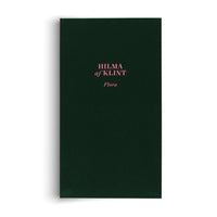 A hardcover book with a dark green fabric cover, standing upright against a white background. In the center, the name HILMA af KLINT and the title Flora are printed in a delicate pink font.