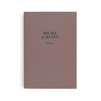 A book with a solid, mauve-brown cover is shown vertically against a white background. The text HILMA af KLINT Flora is printed in the center in a dark green serif and script font.