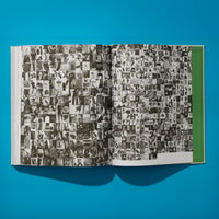An overhead shot of an open book on a bright blue surface. The pages are filled with a dense collage of hundreds of small, black and white photographs arranged in a grid. The outer edge of the right page has a solid green vertical bar. The book casts a dark shadow below it.