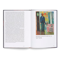 An open art book on a white surface. The left page contains German text, and the right page displays Edvard Munch's painting, Self-Portrait. Between the Clock and the Bed. The painting shows the artist standing in a colorful room between a grandfather clock and a bed with a patterned cover.
